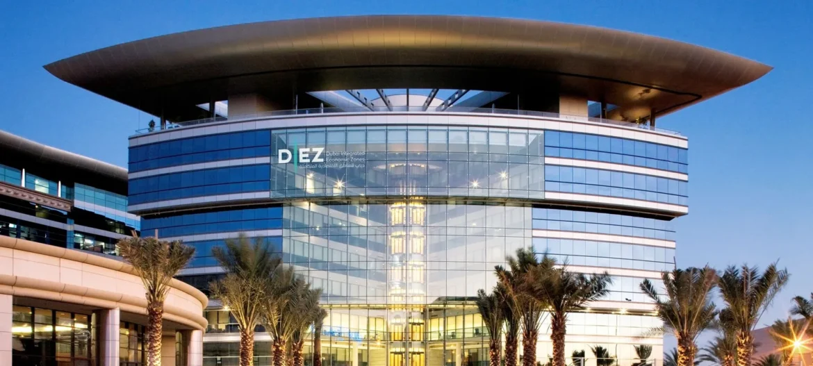 Modern glass office building with a curved rooftop and palm trees in the foreground; sign reads DEZ Dubai Integrated Economic Zones.