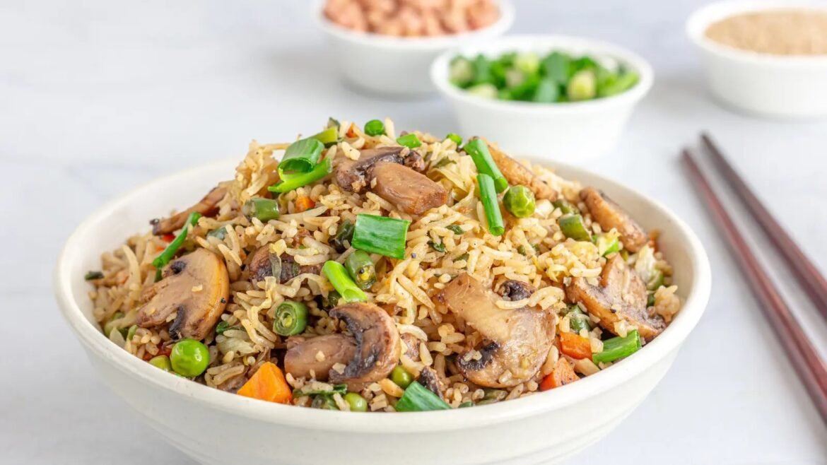Bowl of fried rice with mushrooms, peas, carrots, and green onions, served with chopsticks on the side.