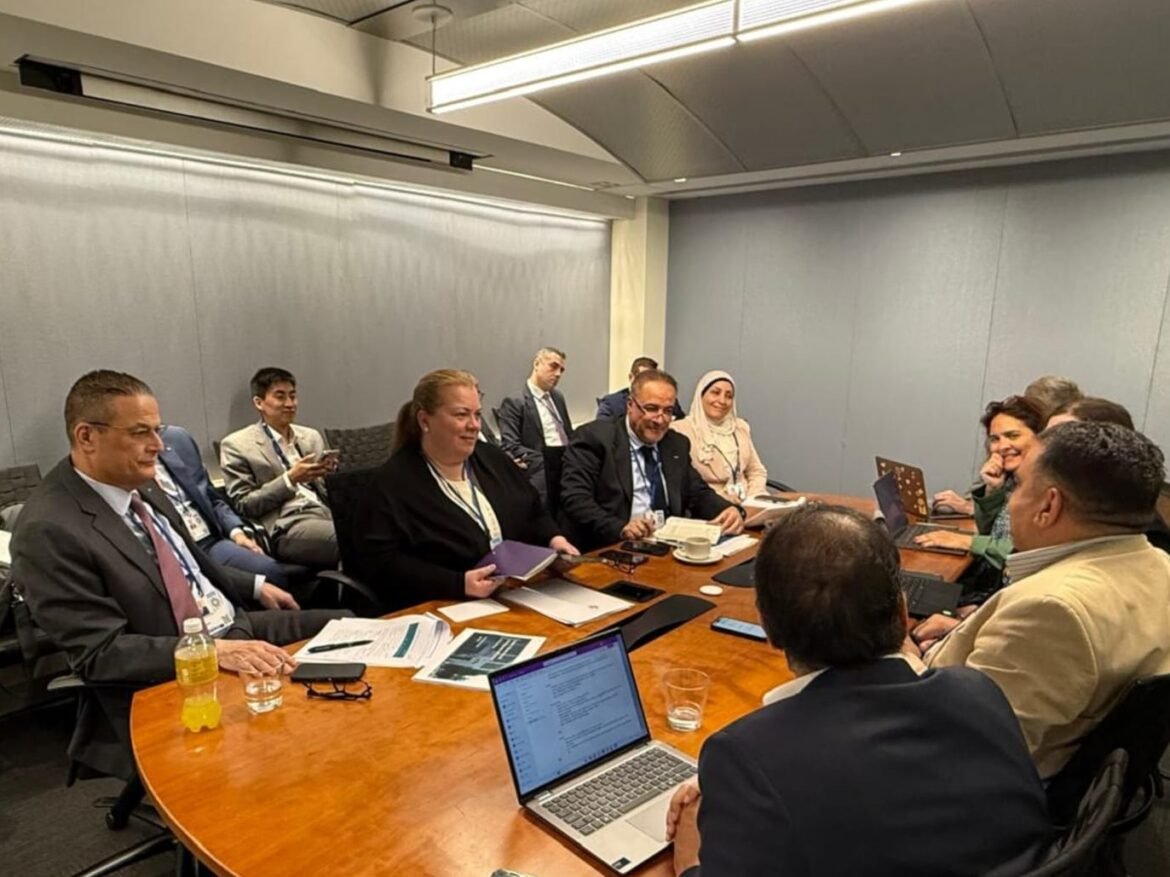 Diverse group of professionals in a boardroom, seated around a wooden table with laptops and documents during a meeting.