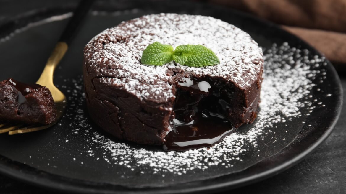 Chocolate lava cake dusted with powdered sugar and a mint garnish, with molten center leaking onto a dark plate.
