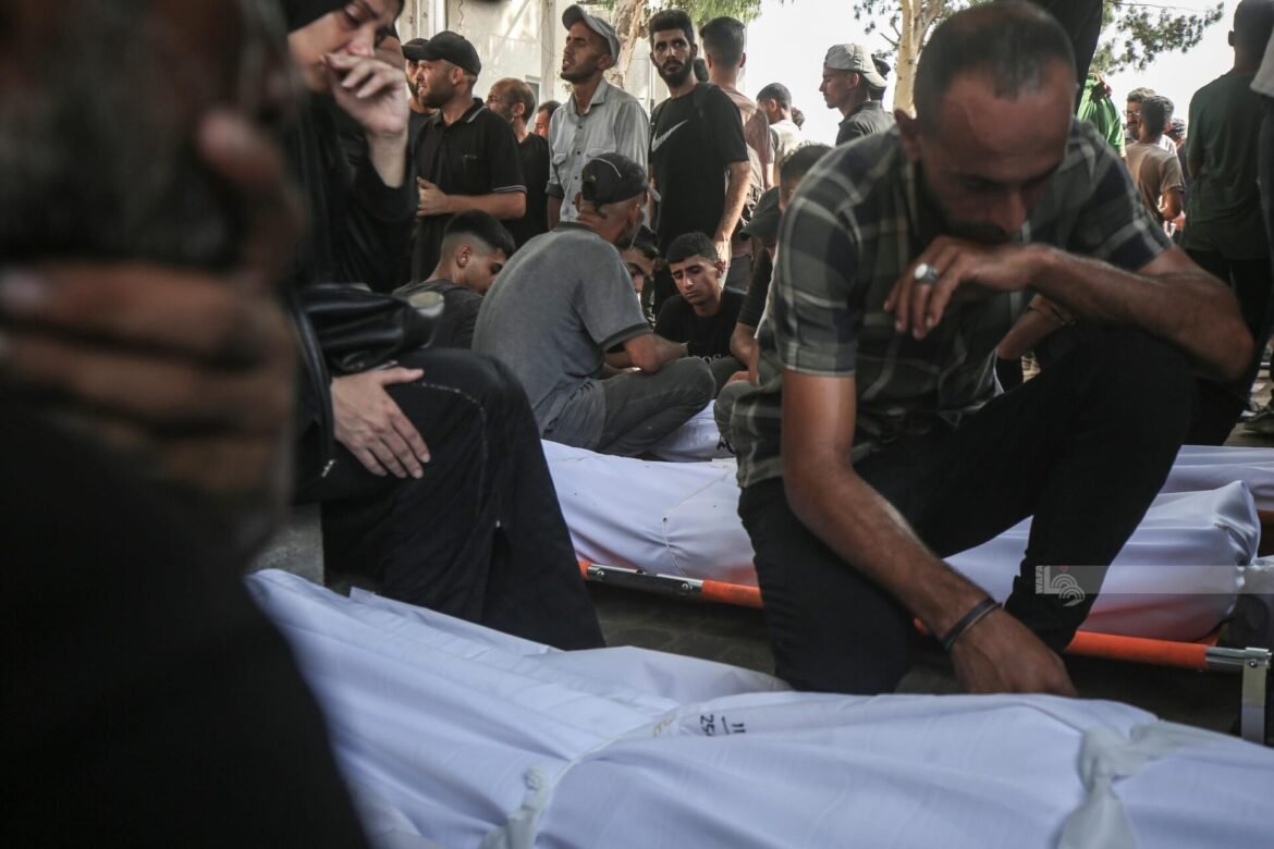 Group of men surrounding a body covered by a white sheet on a stretcher outdoors.