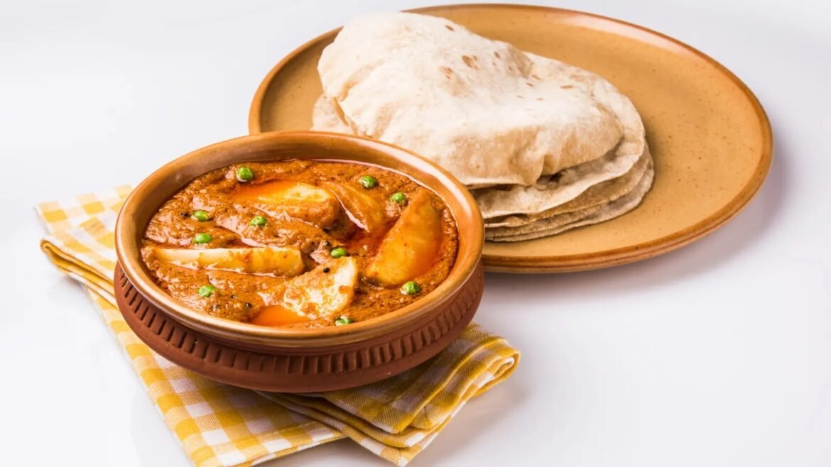 Clay pot curry with potatoes and peas, served with stacked flatbreads on a beige plate.