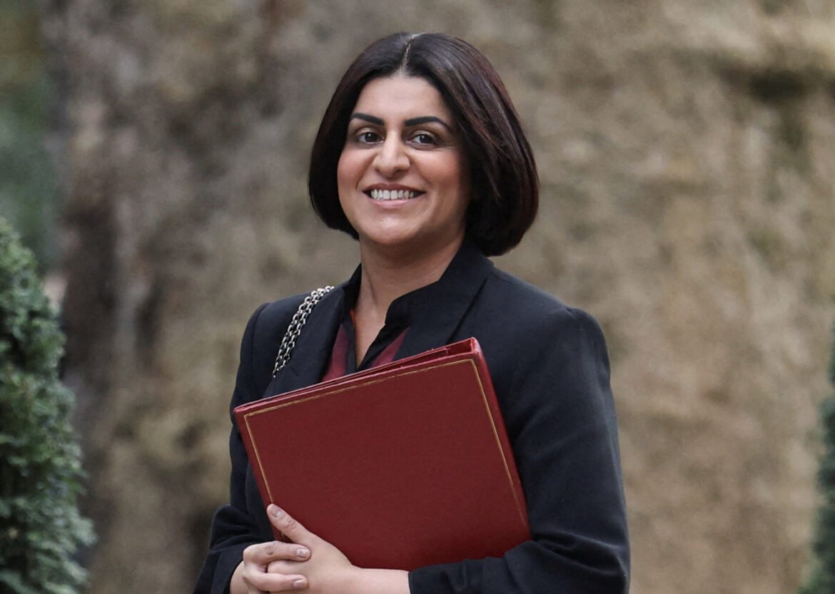 Smiling woman in a dark blazer outdoors, holding a red binder.