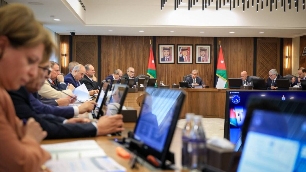 Officials seated around a long conference table in a wood-paneled room, with Jordan flags and portraits on the wall behind them.