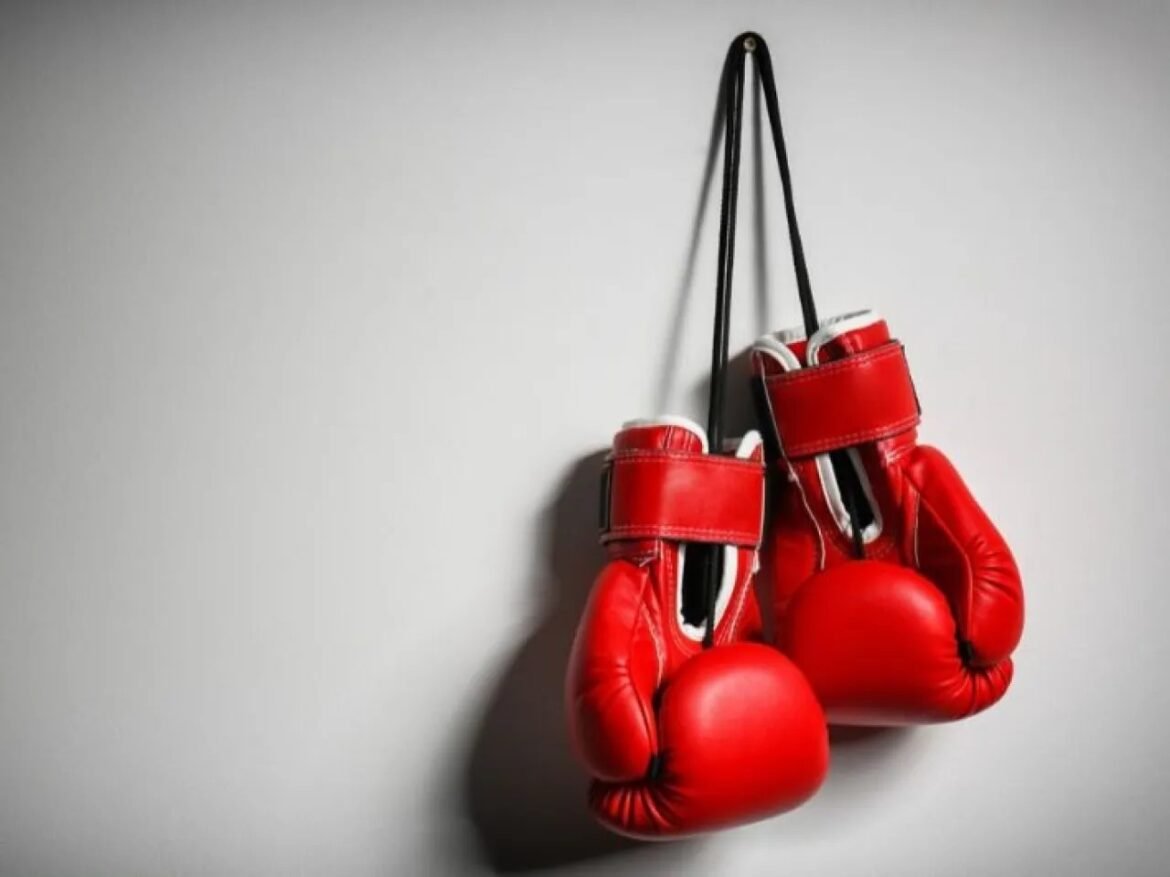 Pair of red boxing gloves hanging by black straps against a light wall, ready for use in a gym.
