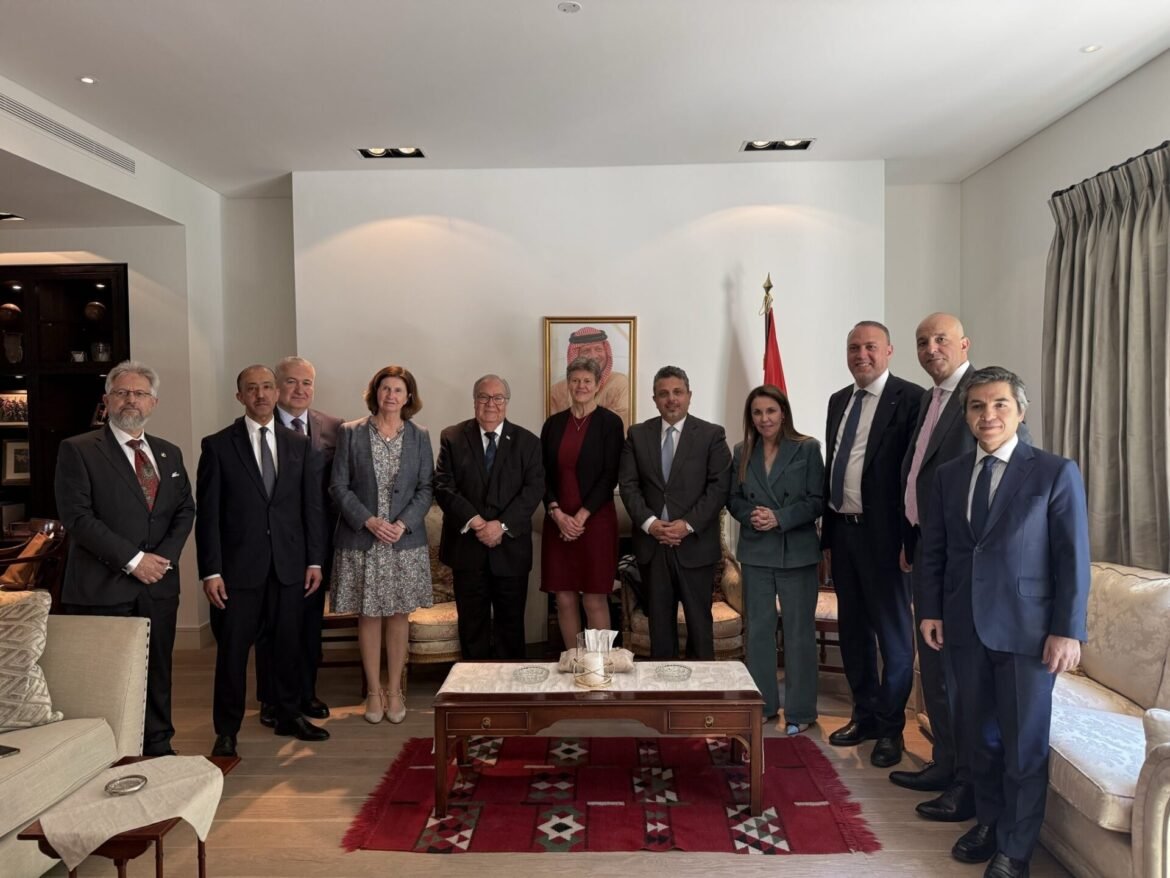 Group of ten formally dressed adults posing for a photo in a living room, with a framed portrait and a red flag visible in the background.