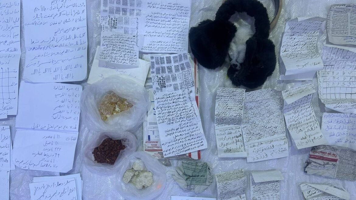 Pair of black earmuffs among scattered handwritten Arabic notes and small bags containing rocks on a light surface; a cluttered display of handwritten pages and specimens.