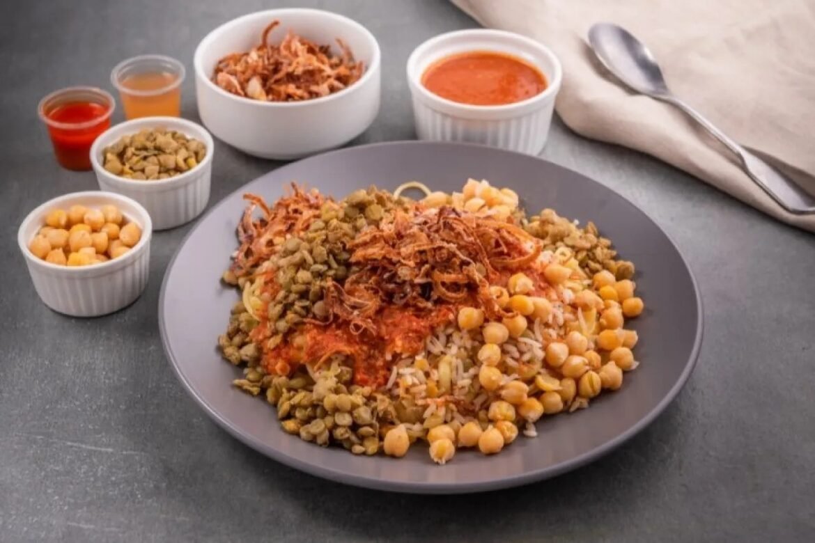 Plate of pasta topped with crispy onions, chickpeas, and lentils, with tomato sauce and small bowls of toppings on a dark table.