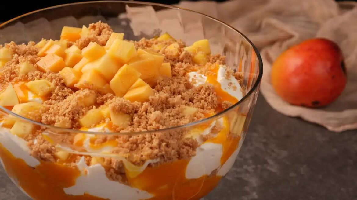 Glass bowl peach crumble dessert with diced peaches, cream, and streusel topping; a whole peach in the blurred background.