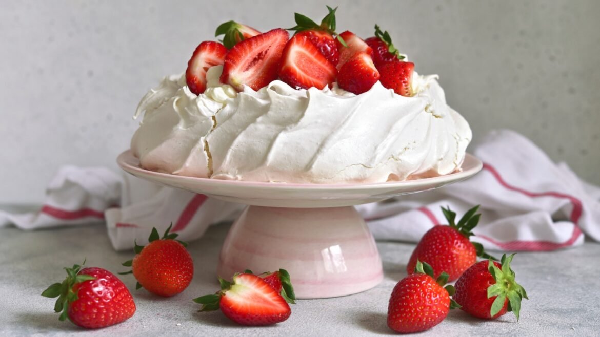 Pavlova with whipped cream and fresh strawberries on a pink cake stand, with strawberries scattered around the base.