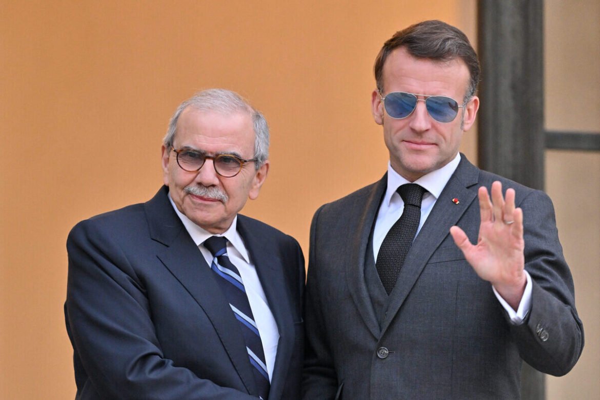 Two men in suits posing for a photo; the man on the right wears sunglasses and waves his hand.