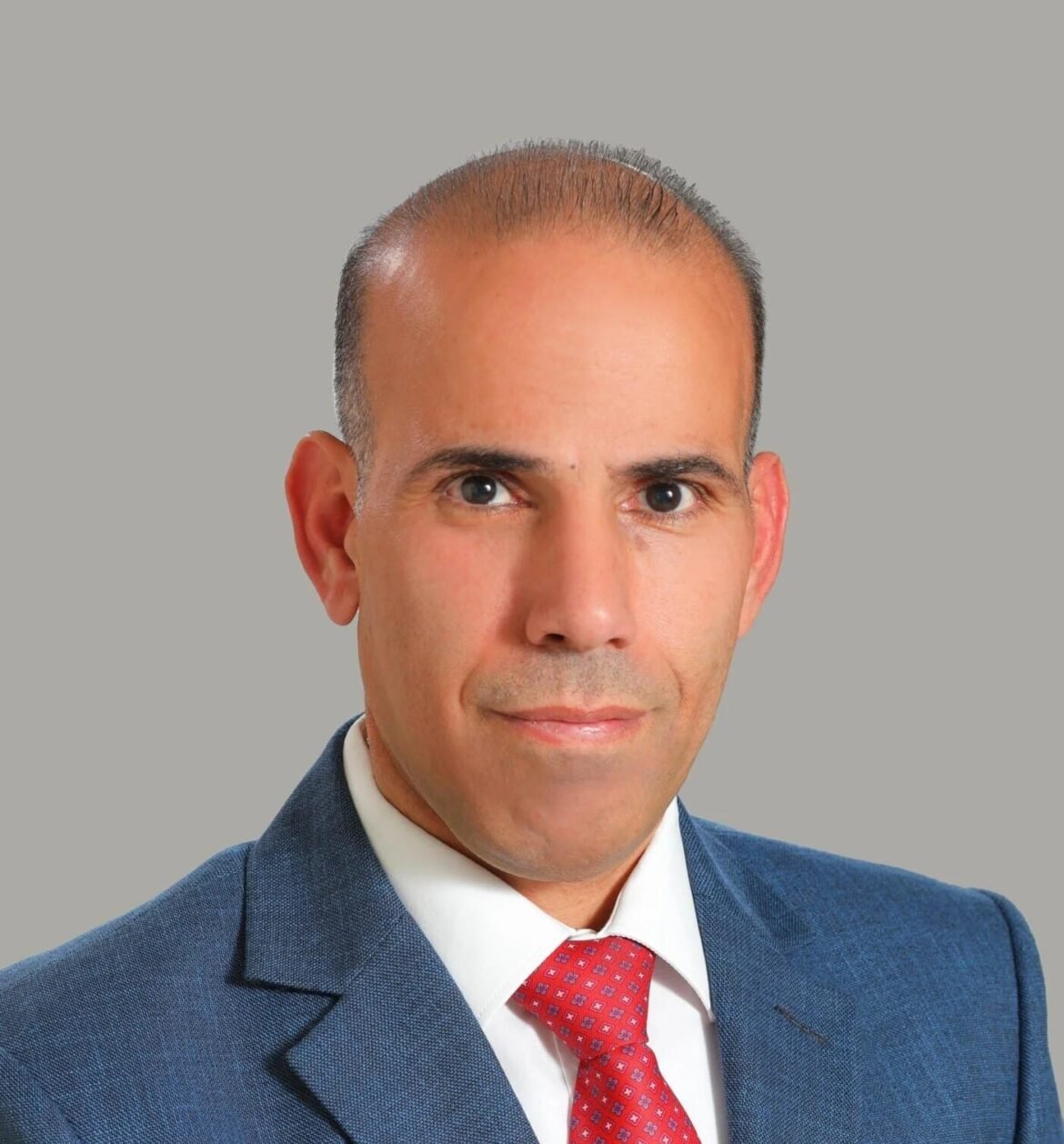 Professional head-and-shoulders portrait of a man in a blue suit and red tie, looking at the camera.