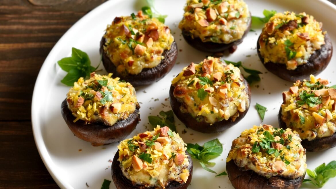 Baked stuffed mushrooms topped with melted cheese, chopped nuts, and herbs on a white platter.