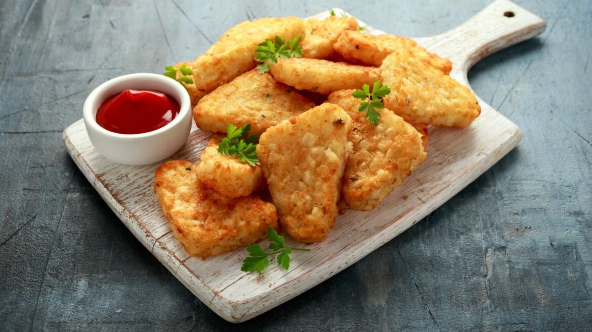 Crispy fried potato bites with parsley garnish on a wooden board and a small bowl of ketchup on the side.