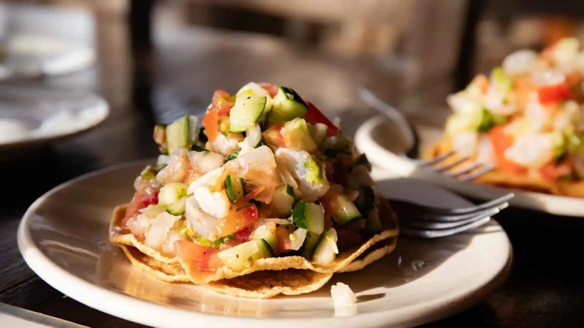 Tostada topped with chunky pico de gallo-style salsa (tomato, cucumber, onion) on a plate in a restaurant setting