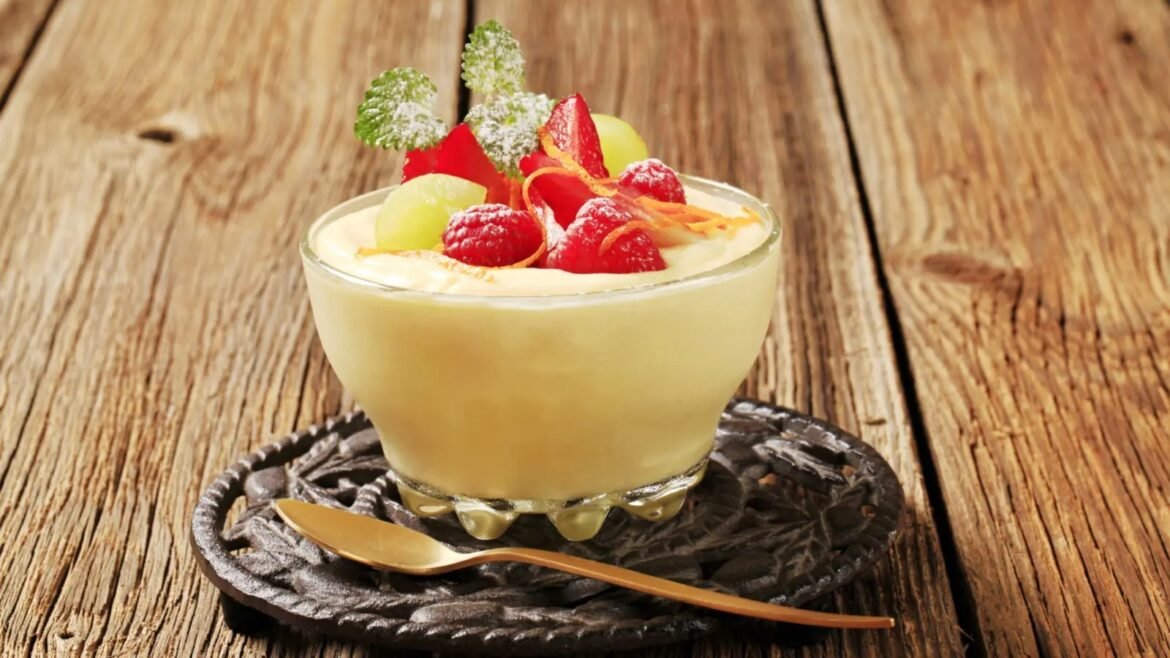 Creamy dessert cup topped with raspberries, grapes, mint, and citrus zest on a rustic wooden table