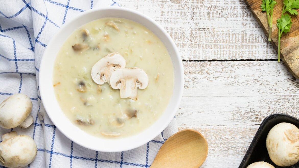 Creamy mushroom soup in a white bowl topped with sliced mushrooms on a rustic wooden table