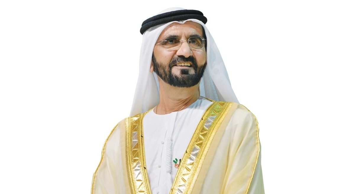 Man in traditional white kandura with a gold-trimmed bisht and black agal, smiling against a white background.