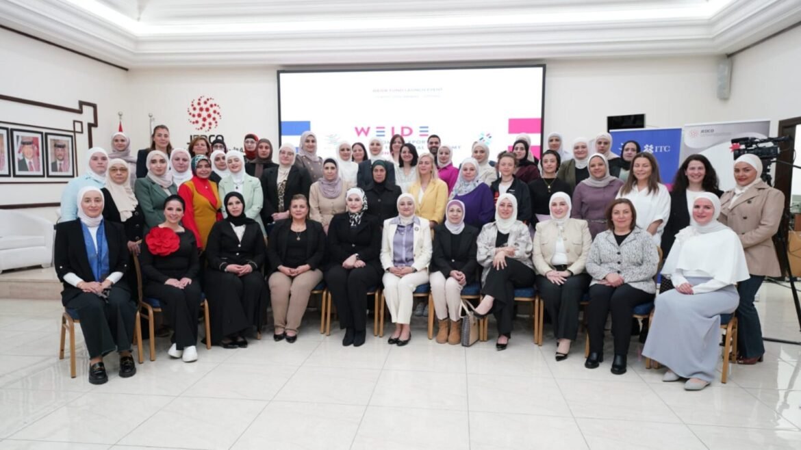 Group of women, many wearing hijabs, posing for a large group photo in a conference room with banners and framed portraits on the wall.