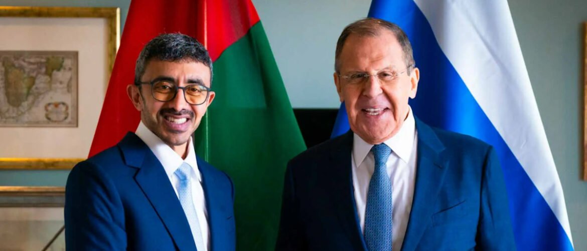 Two men in suits pose for a formal photo, with national flags in the background.