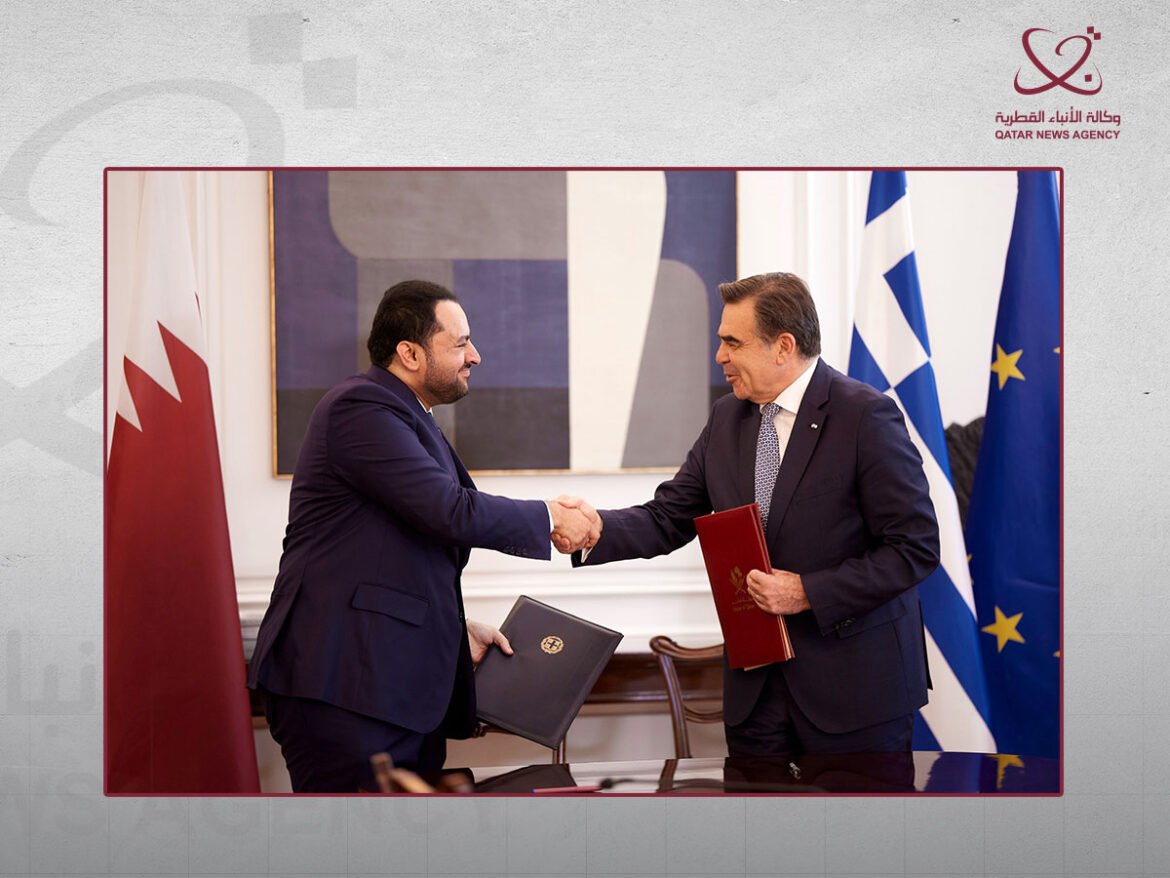 Two men in dark suits shake hands at a signing ceremony, each holding a folder, with flags in the background (Qatar and EU).