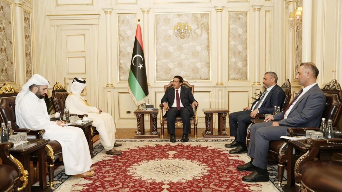 Official meeting in an ornate room; central man in a suit sits with Libyan flag beside him, others in chairs along the sides.