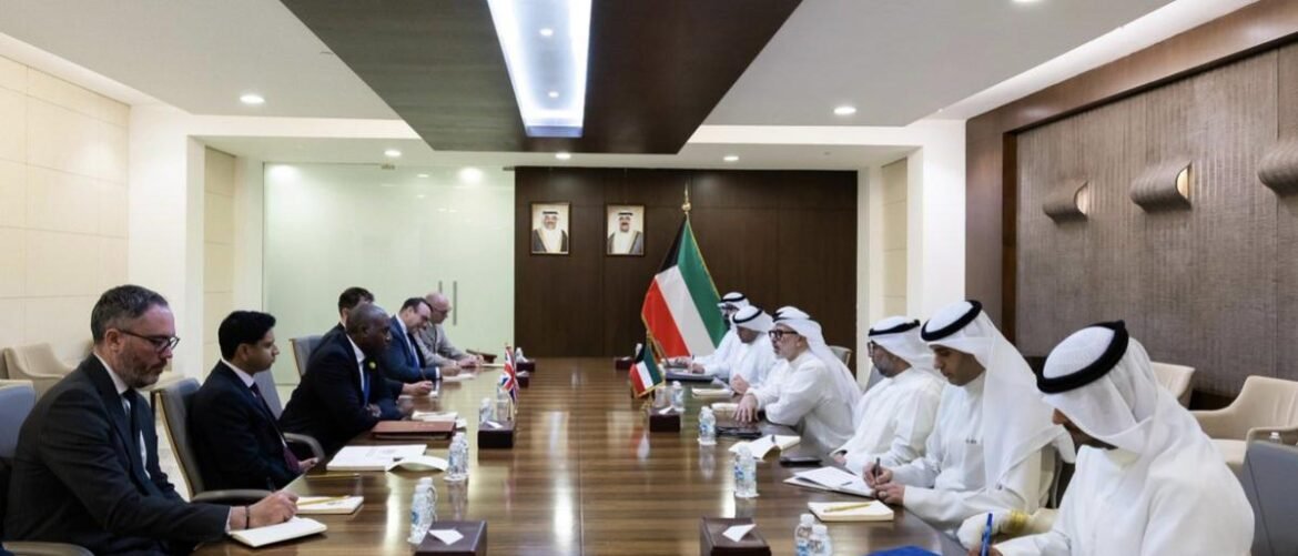 Diplomatic meeting in a boardroom with Kuwaiti flag between delegations, attendees in suits and kanduras.