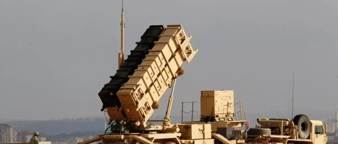 Mobile missile launcher mounted on a tracked vehicle, with a tall, angled rack of rocket pods raised skyward; soldier visible in distance.