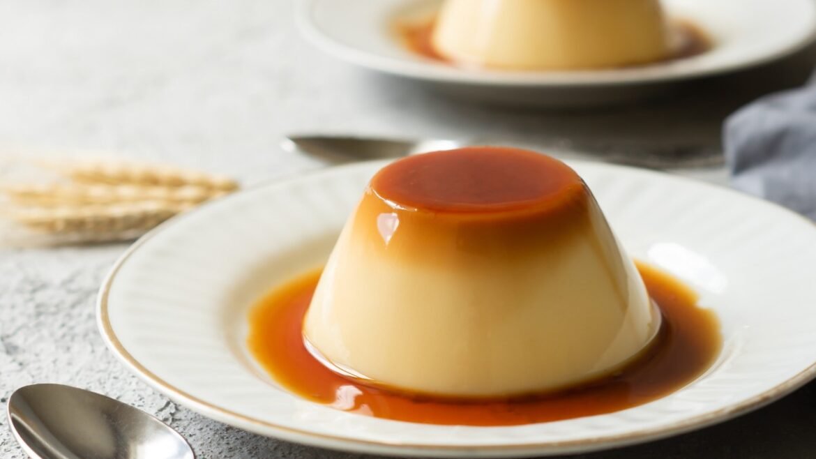 Creamy flan with caramel sauce on a white plate, caramel ring around the dessert on a rustic table.