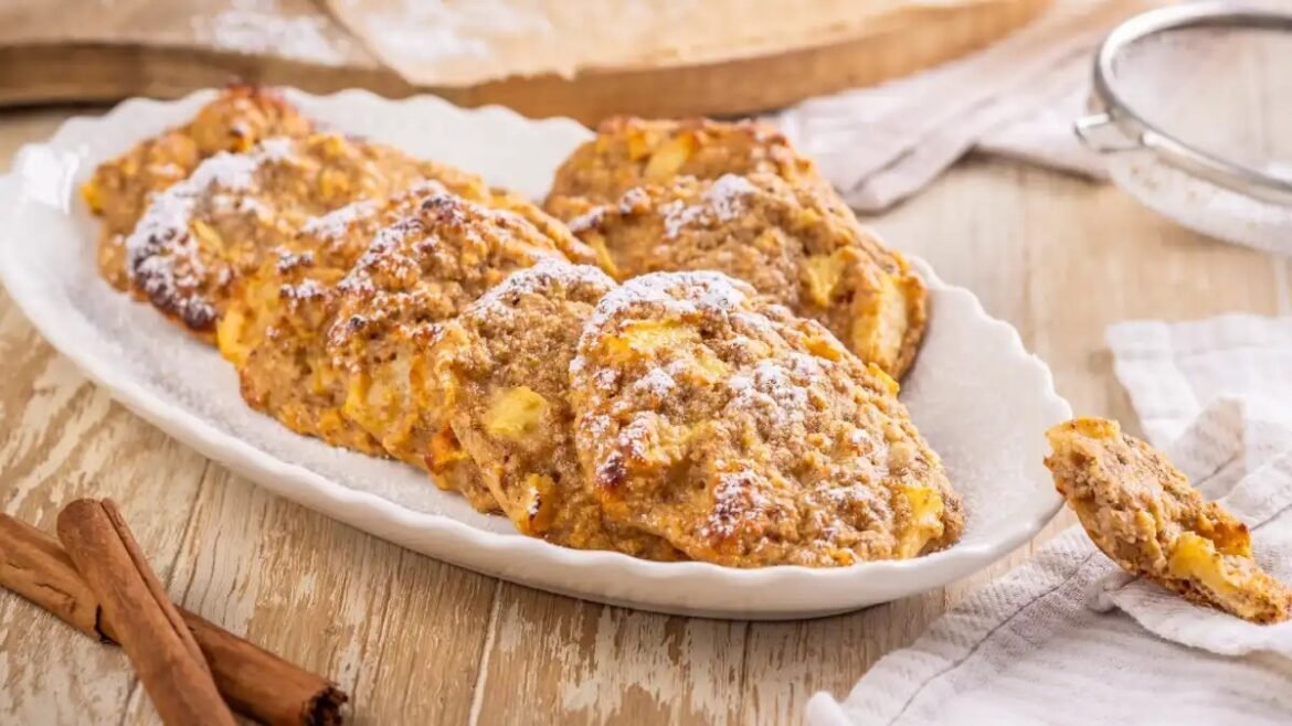 Plate of homemade peach-filled cookies dusted with powdered sugar on a rustic wooden table, with cinnamon sticks nearby.