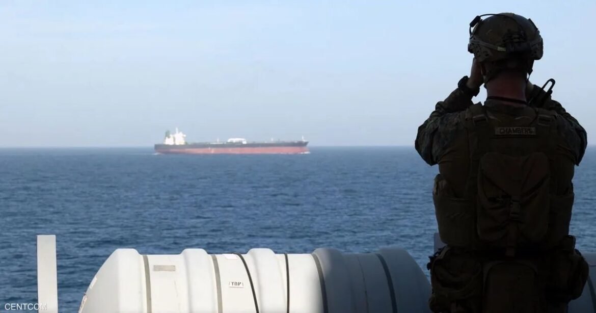 Military personnel in tactical gear on a ship deck watches a distant cargo vessel on the sea, horizon calm.