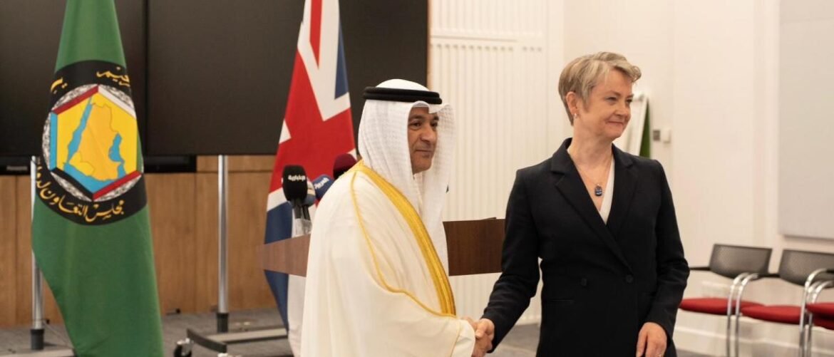 Diplomat in a white traditional robe shakes hands with a woman in a black suit at a formal briefing, flags in the background.