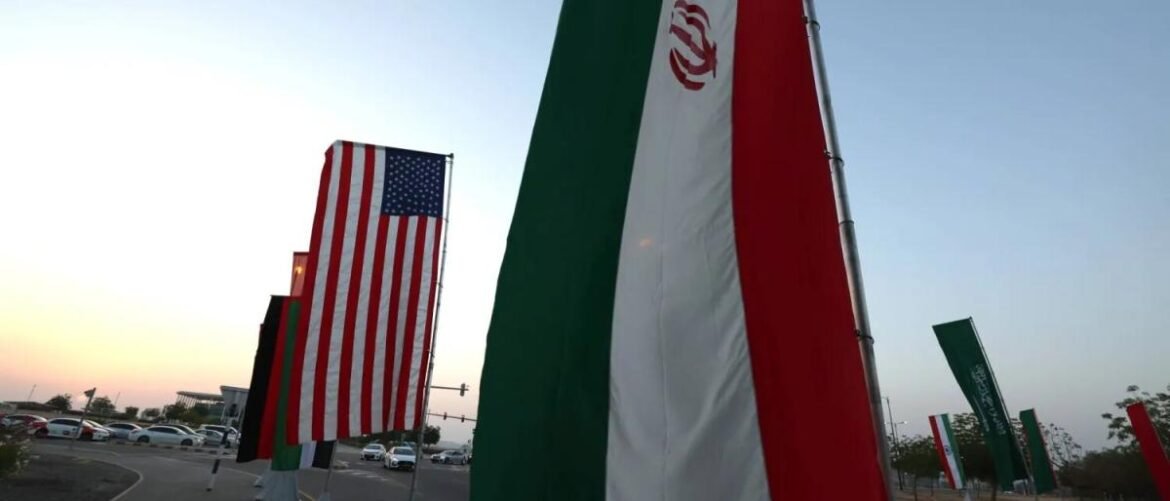 Row of tall national flags, including the United States and Iran, lined along a street at sunset.