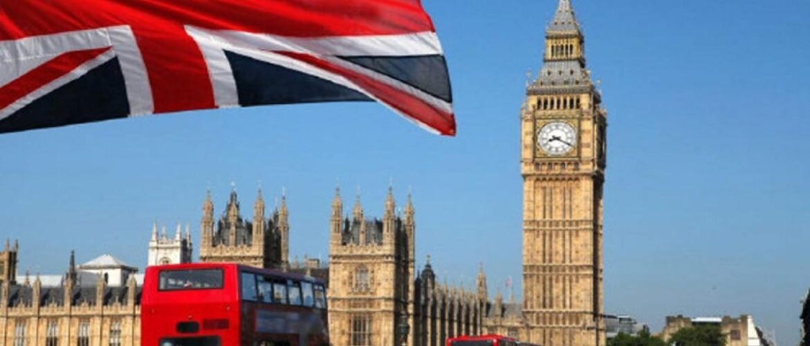 Union Jack flag waves above the Palace of Westminster with Big Ben and a red double-decker bus in London
