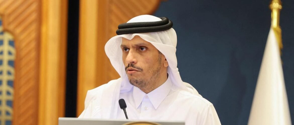 Man in a white thobe and headscarf speaks at a podium with a microphone at a formal event.