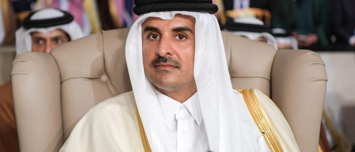 Man in traditional Arab attire (thawb and headscarf) seated in a beige chair at a formal event.