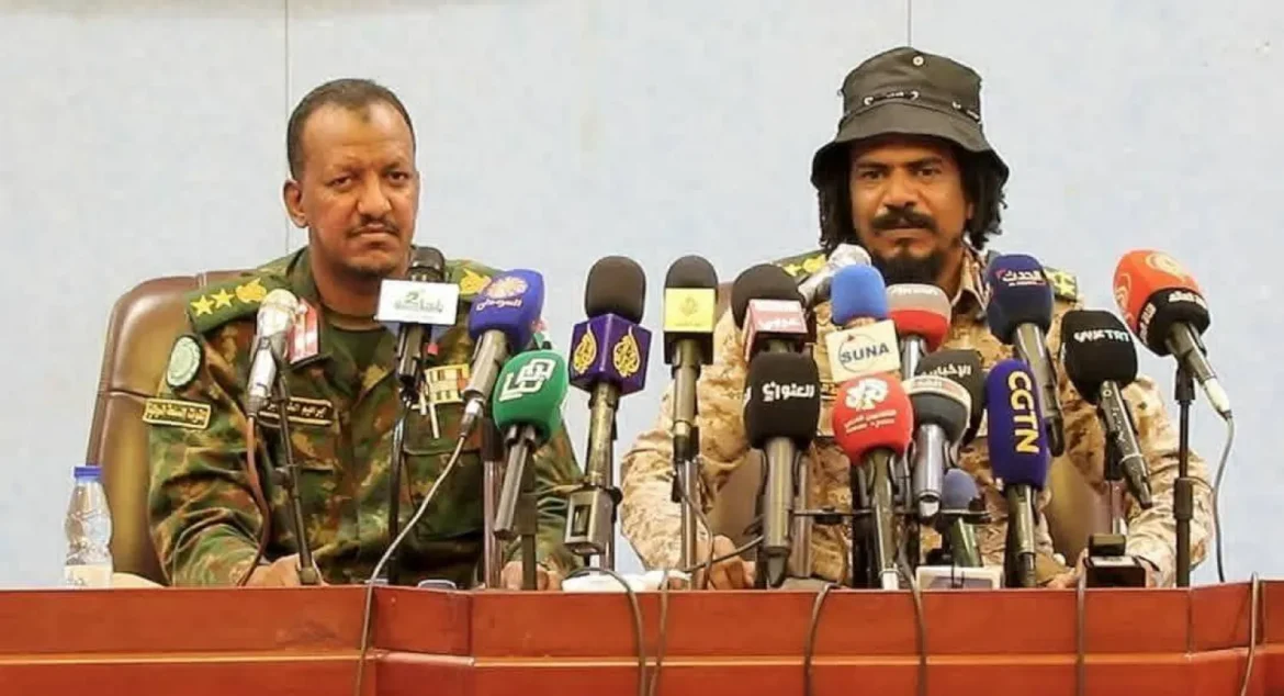 Two men in military uniforms sit behind a row of microphones at a press conference.