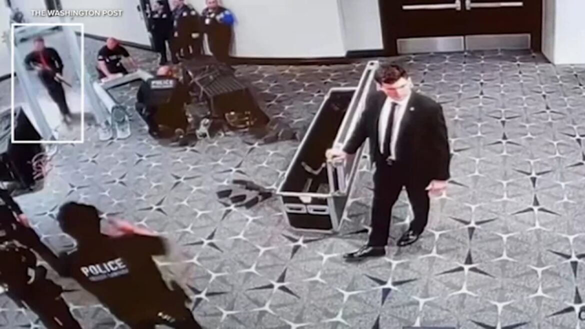 Surveillance image in a hotel lobby: a man in a suit near an escalator as police approach from the left; a highlighted figure stands near the glass elevator.