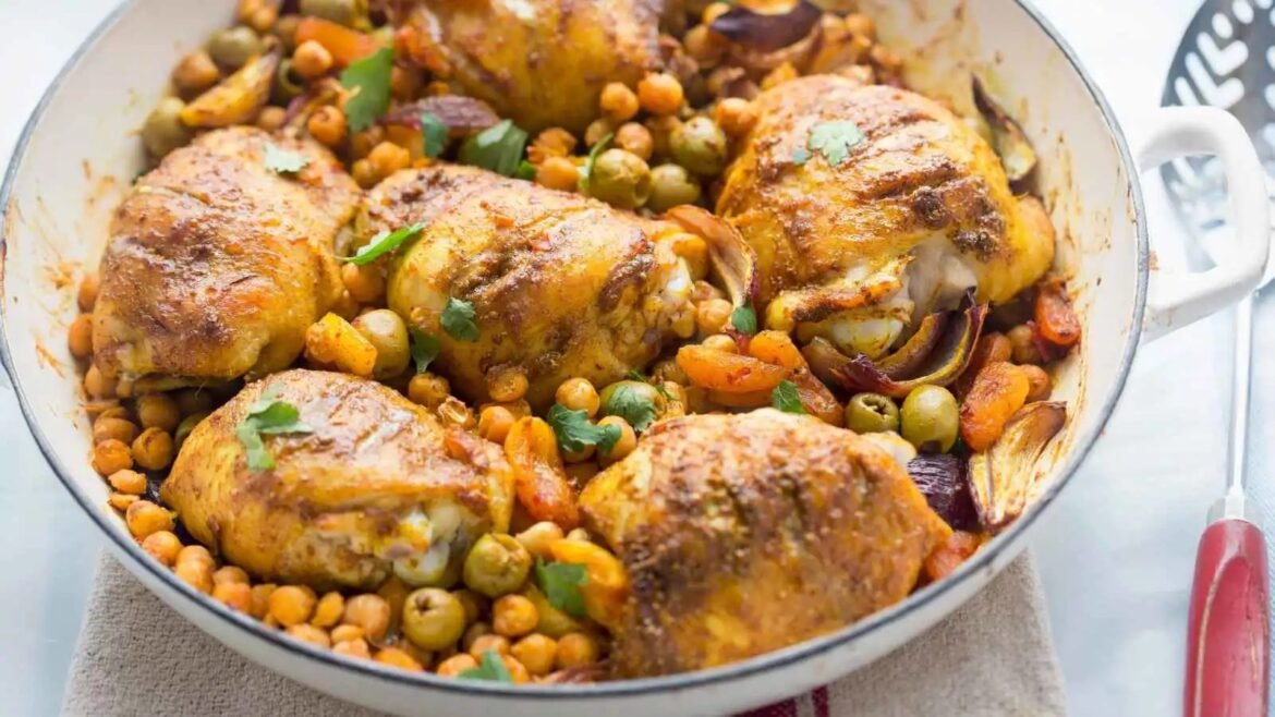 Skillet with seasoned roasted chicken thighs, chickpeas, olives, and carrots in a tomato-spiced sauce, garnished with herbs