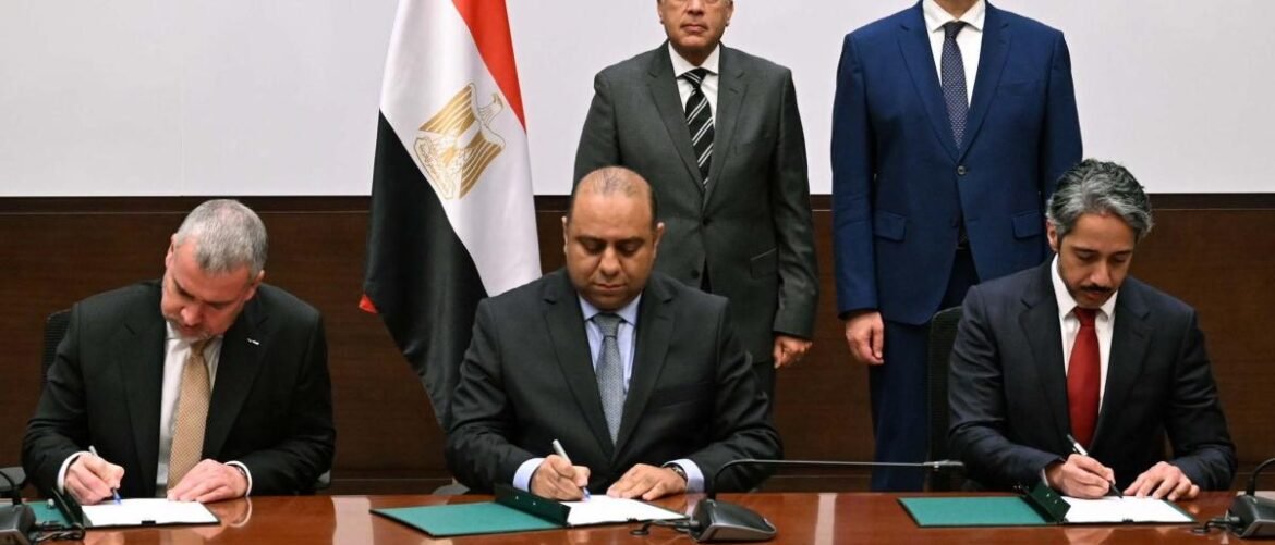 Three businessmen seated at a polished conference table sign documents, with an Egyptian flag behind them and two others standing in suits.