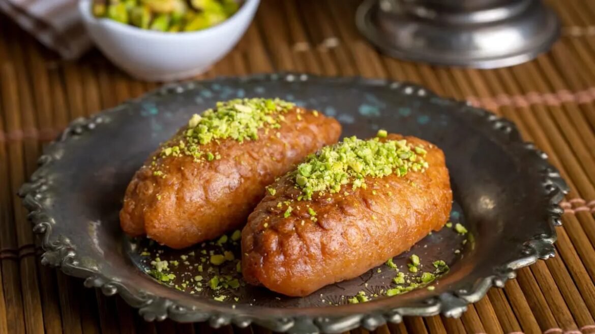Two fried pastries arranged on a dark decorative plate, topped with chopped pistachios.