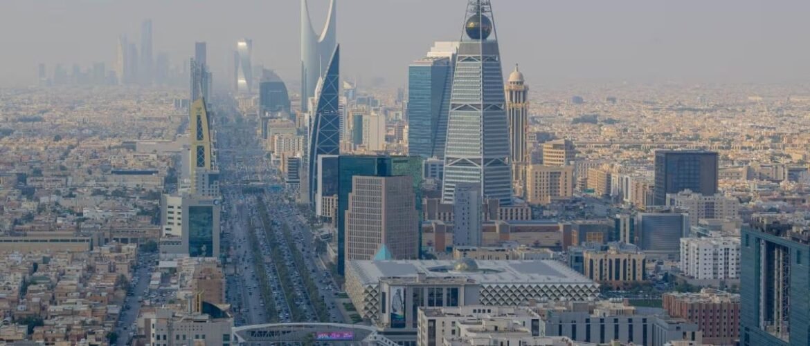 Aerial view of Riyadh's skyline with modern high-rises, including the Kingdom Centre and Al Faisaliah Tower in the foreground.