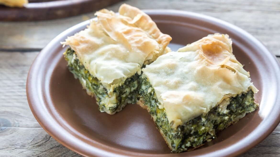 Two triangular pieces of spanakopita (spinach and feta filo pie) on a brown plate, showing flaky golden pastry and green filling.