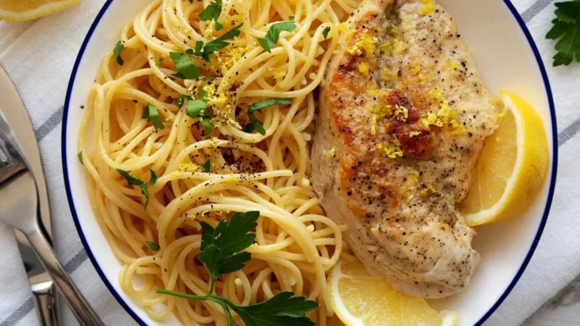 Plate of lemon-pepper chicken served with spaghetti tossed with parsley on a white plate, with lemon wedges on the side.