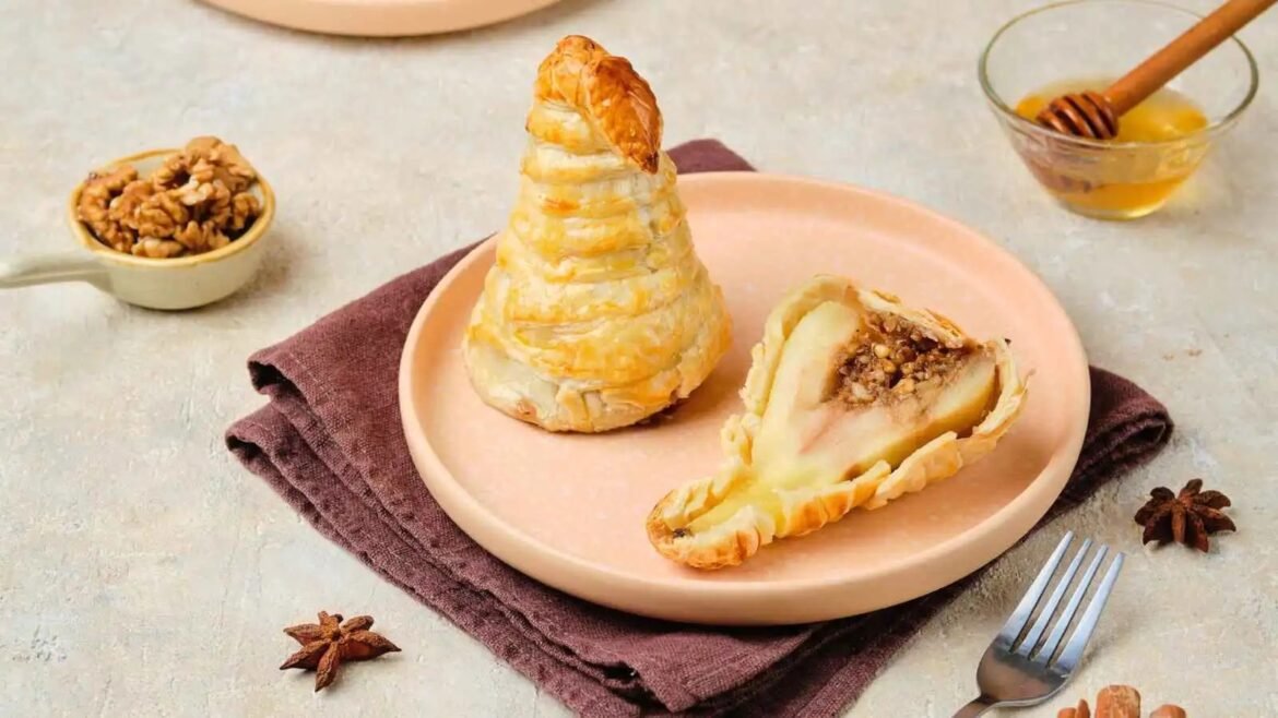 Flaky puff pastry cone and a filled pastry slice on a pink plate, with walnuts, honey and a fork nearby.