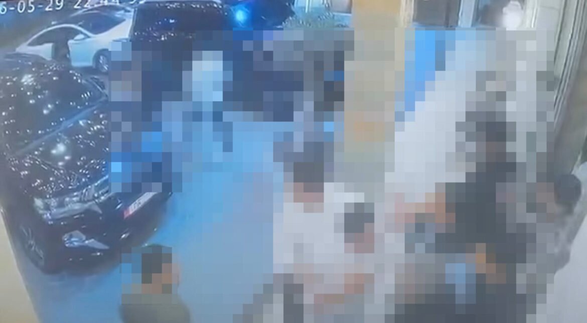 Security camera still showing blurred figures indoors near a doorway with parked cars visible outside, blue-tinted lighting.