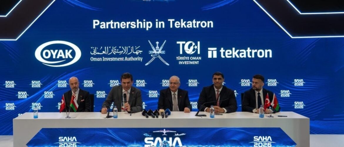 Five men in suits sit at a long white table on a stage, microphones and water bottles in front, as a blue backdrop reads 'Partnership in Tekatron' with sponsor logos."