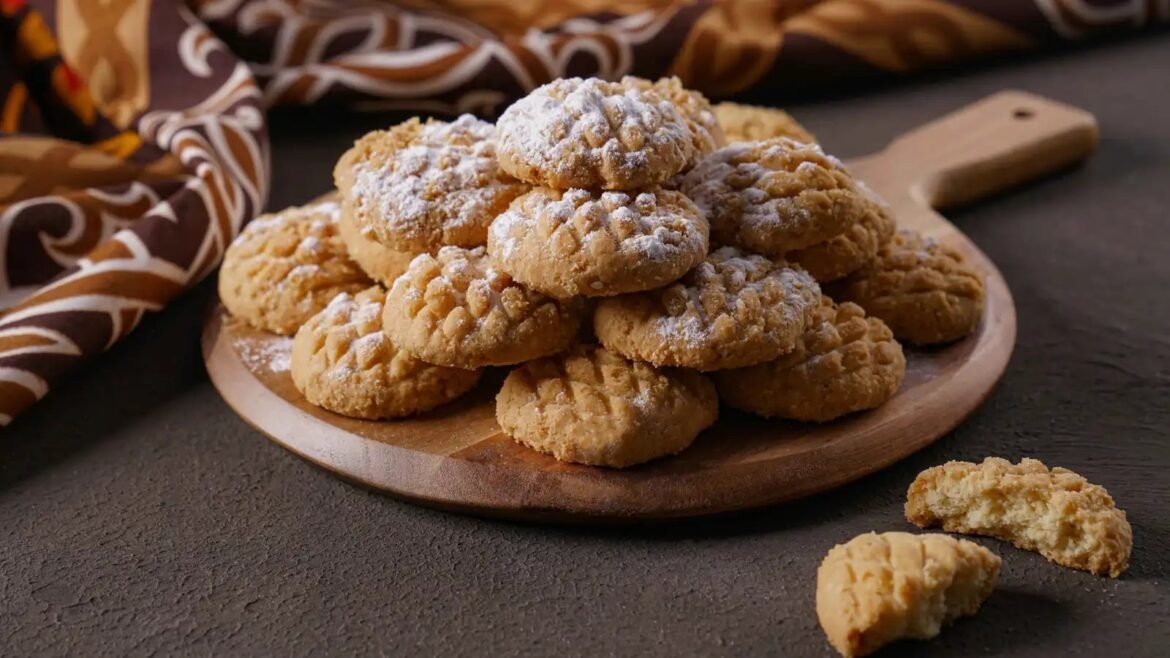 Stack of sugar-dusted walnut cookies piled on a round wooden board, with a patterned cloth in the background.