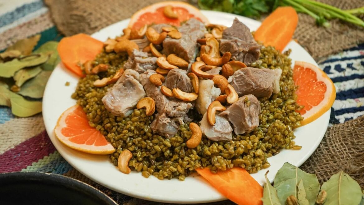 Lamb chunks with cashews on a bed of cooked lentils, citrus garnish on a white plate.