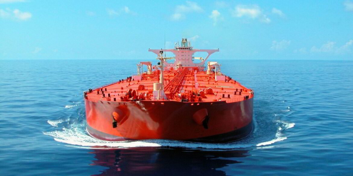 Red oil tanker sailing in calm blue ocean, wake visible behind the hull